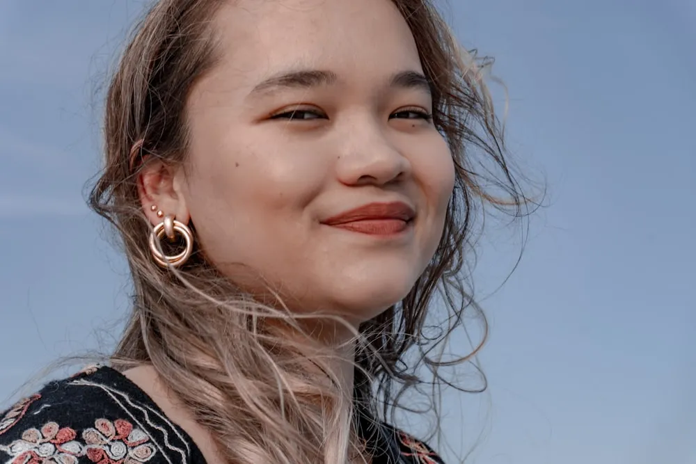 A young woman smiling against a clear blue sky.